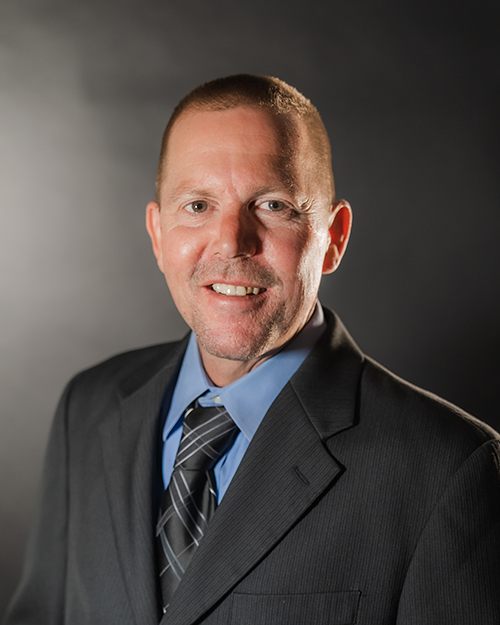 Professional man from the QT Executive Team in suit and tie posing against a dark backdrop.