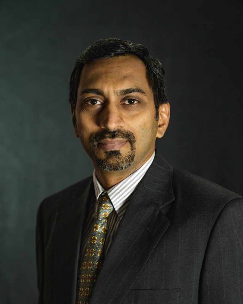 A professional portrait of a man from the QT Executive Team in a suit and tie against a dark backdrop.