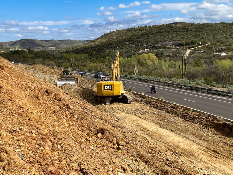 Construction equipment operating on a Flex Lane hillside near the I-17 under a cloudy sky.