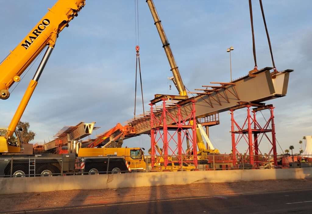 Construction cranes installing large bridge segments at a construction site during sunset, as part of Civil Engineering Services.