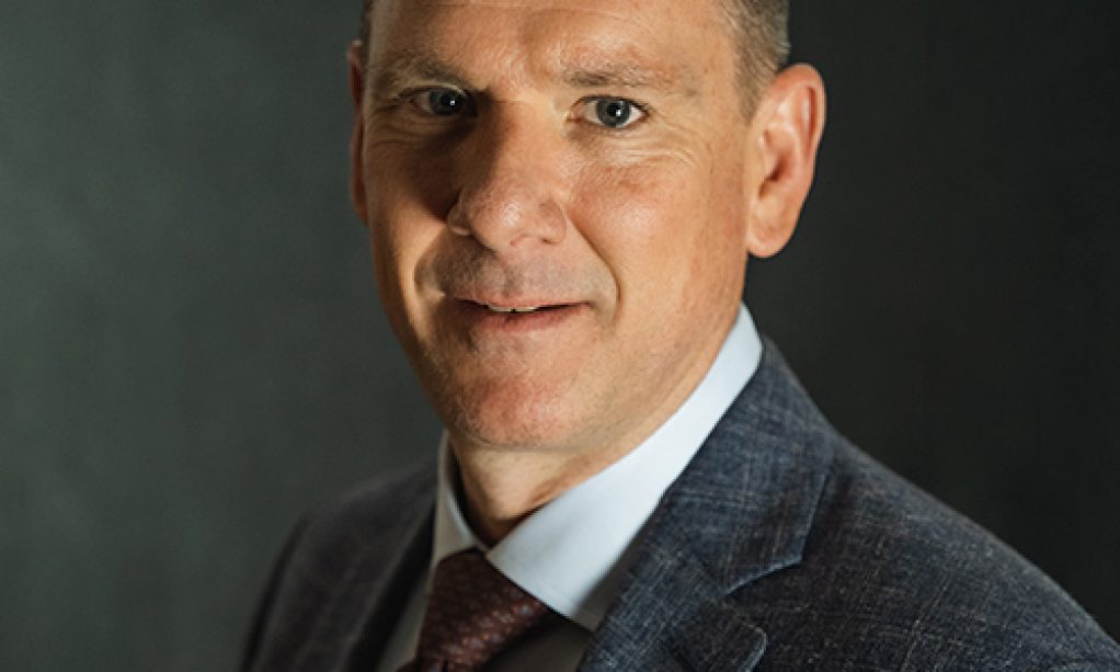 A professional man in a suit, from the QT Executive Team, posing for a formal portrait against a dark background.